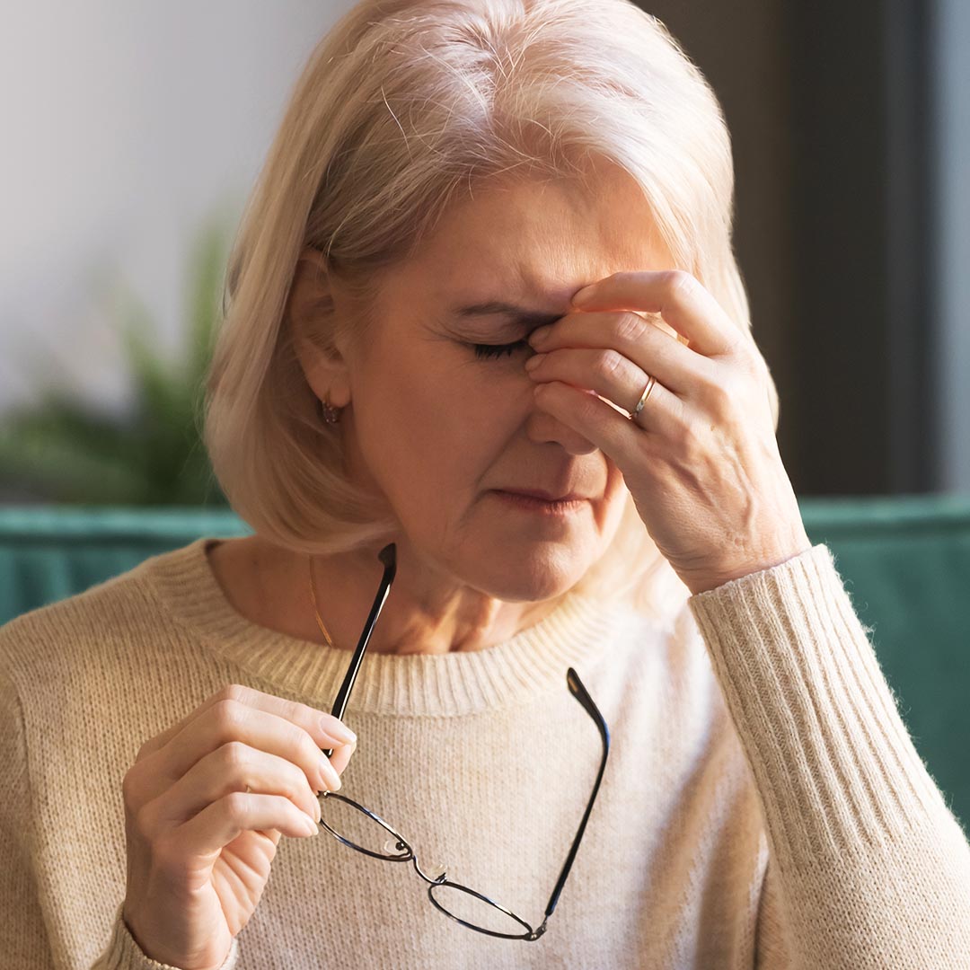 Woman holding her glasses and rubbing her forehead