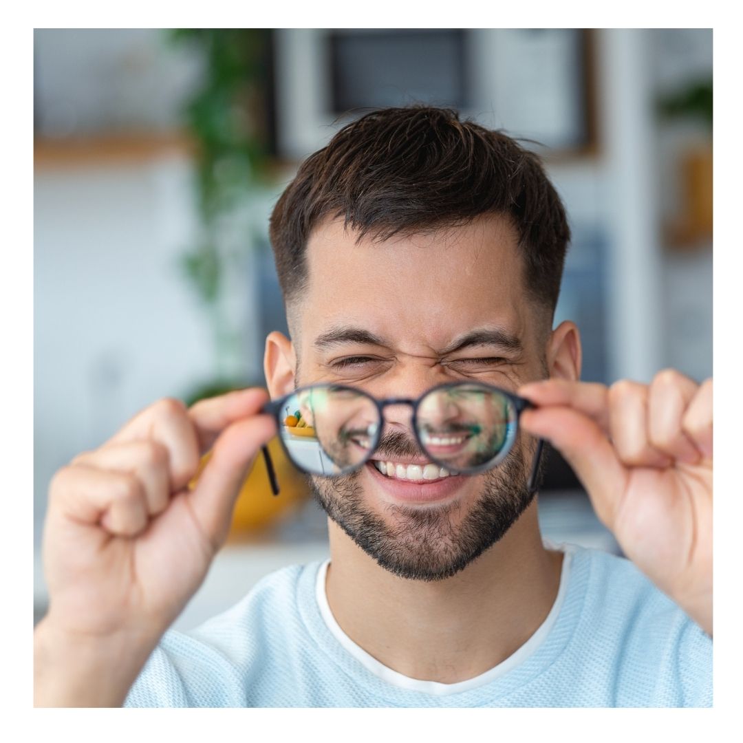 man squinting holding up glasses to face