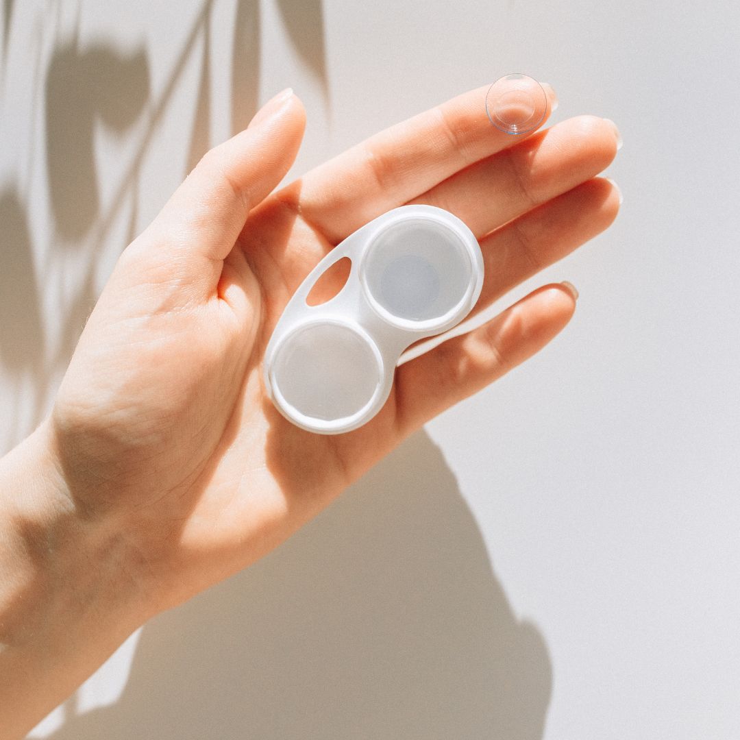 A hand holding a contact lens case with a lens on a fingertip.