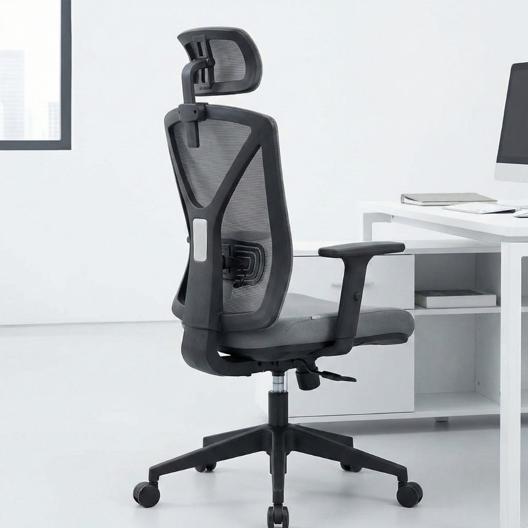 A full view of a modern, grey ergonomic office chair with a headrest and lumbar support, placed next to a white desk.