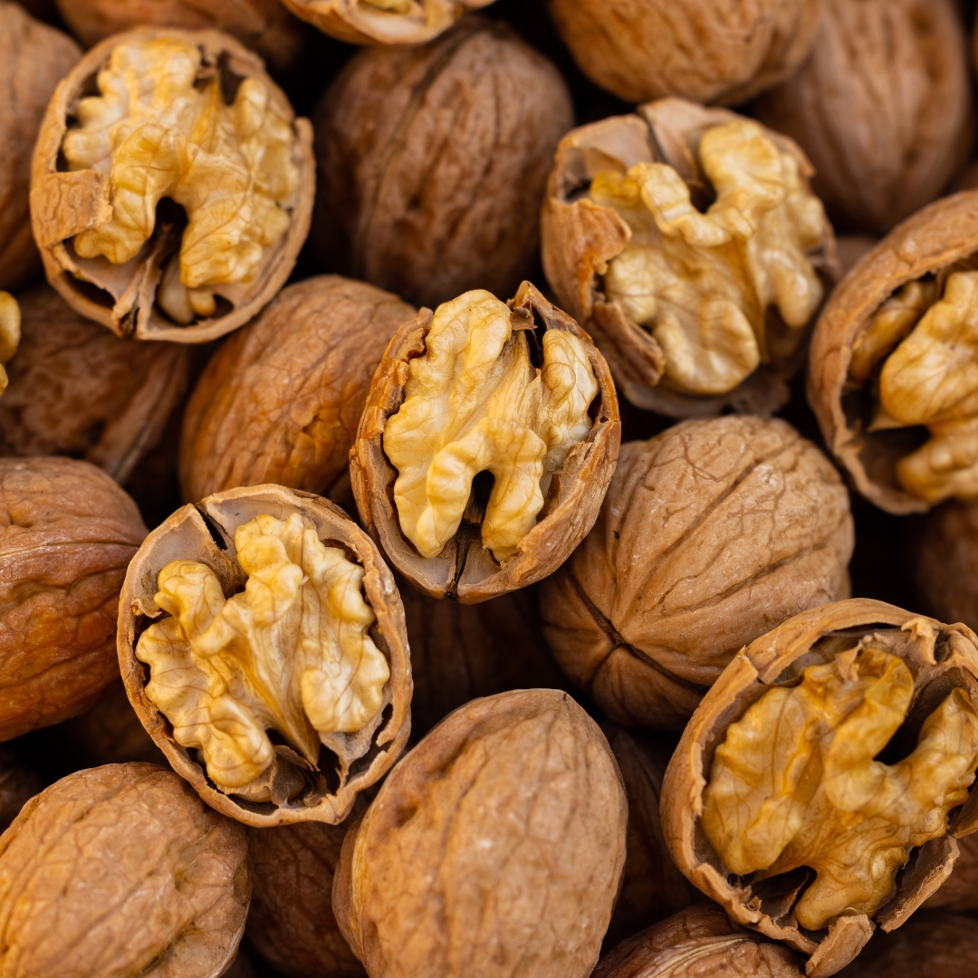 A detailed close-up shot shows a collection of whole and cracked walnuts, highlighting their natural texture and healthy kernels.