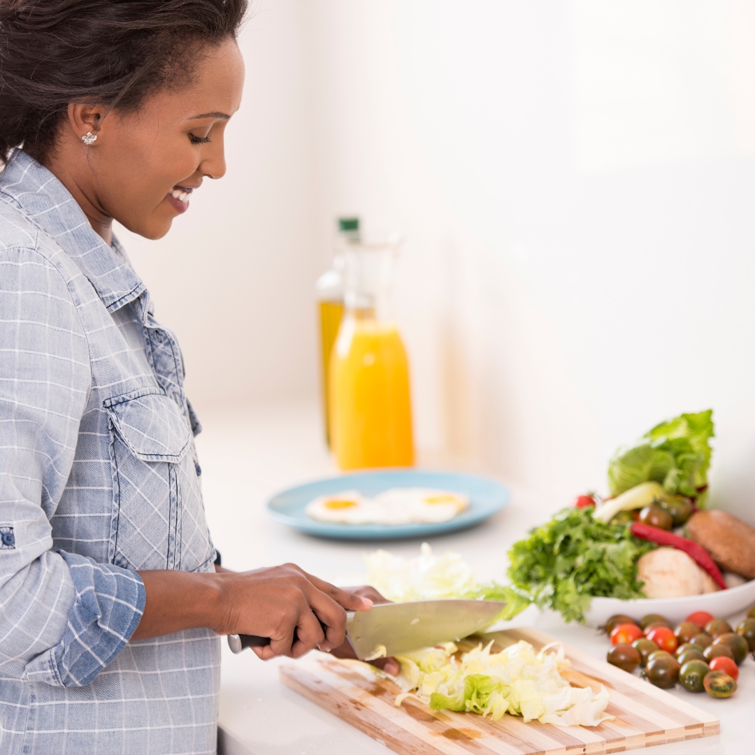 A smiling woman prepares fresh vegetables on a wooden cutting board in a bright, modern kitchen.